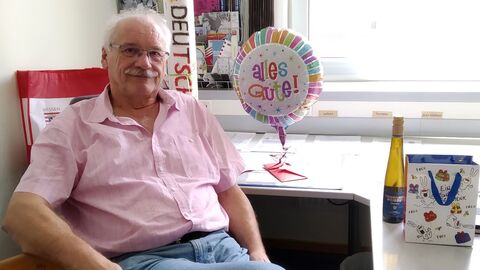 Uwe Josuttis, Leiter der regionalen Geschäftsstelle Nordhessen, wird in den Ruhestand verabschiedet.  Uwe Josuttis, ehemaliger Leiter der Geschäftsstelle, sitzt an seinem Schreibtisch. Im Hintergrund stehen Präsente wie eine Flasche Wein und ein Luftballon mit dem Text "Alles Gute"