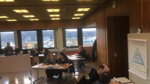 Teilnehmer und Teilnehmerinne der Prozessentwicklungsgruppe sitzen zu zweit an Tischen und arbeiten an Plakaten.