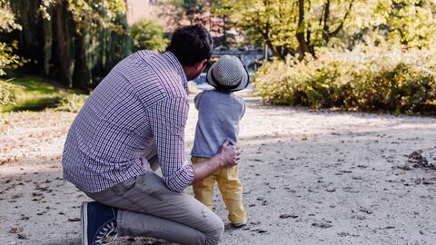 Vater und Kind Vater kniet neben seinem Kind und zeigt auf ein Ziel im Hintergrund. Das Kind folgt seinem Blick.