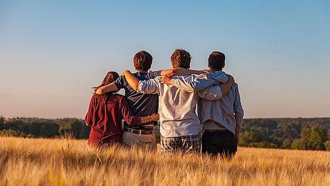 Vier Personen stehen dem Betrachter mit ihren Rücken zugewandt in einem Getreidefeld.