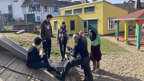 Teilnehmerinnen und Teilnehmer des Basisworkshops im Garten bei der Erstellung eines Bilderbuchs. Hier an der Rutsche.
