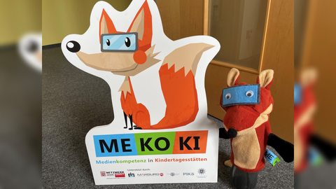 Pappaufsteller MEKOKI und MEKOKI Sympathiefigur stehen nebeneinander auf dem Boden