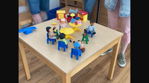Auf einem Tisch stehen Spielfiguren und dazugehörige Spielzeugmöbel.