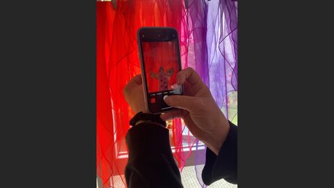 Mit einem Smartphone wird ein gemaltes Feenbild fotografiert. Im Bildhintergrund sind bunte Tücher.