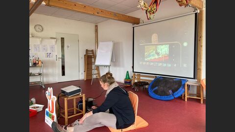 Person sitzt auf dem Fußboden und präsentiert mit Beamer eine Bildgeschichte.