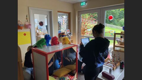 Teilnehmerinnen führen mit Handpuppen ein Rollenspiel durch, das mit einem Tablet gefilmt wird.