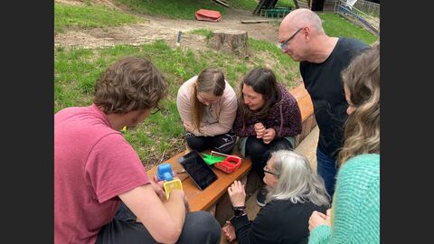 Teilnehmerinen und Teilnehmer bereiten das Rollenspiel mit Sandspielzeug auf einer Bank vor 