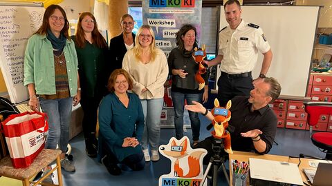 Personengruppe steht vor einen RollUp des Programmes MEKOKI zusammen mit zwei MEKOKI-Handpuppen